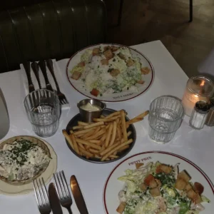 Dækket bord med caesarsalat, pommes frites og levende lys hos Petit Prix
